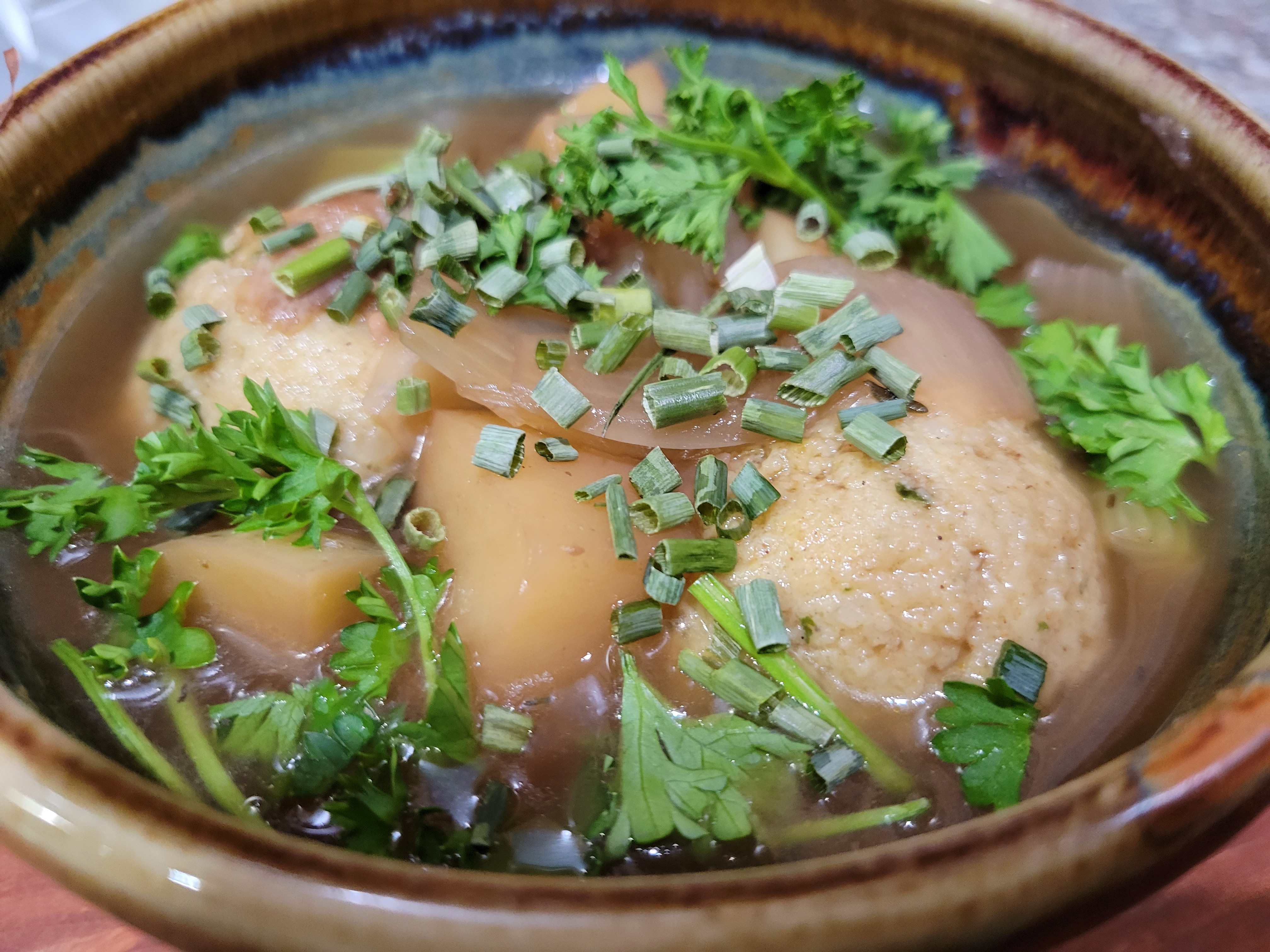 bowl of matzoh ball soup with parsley and chives