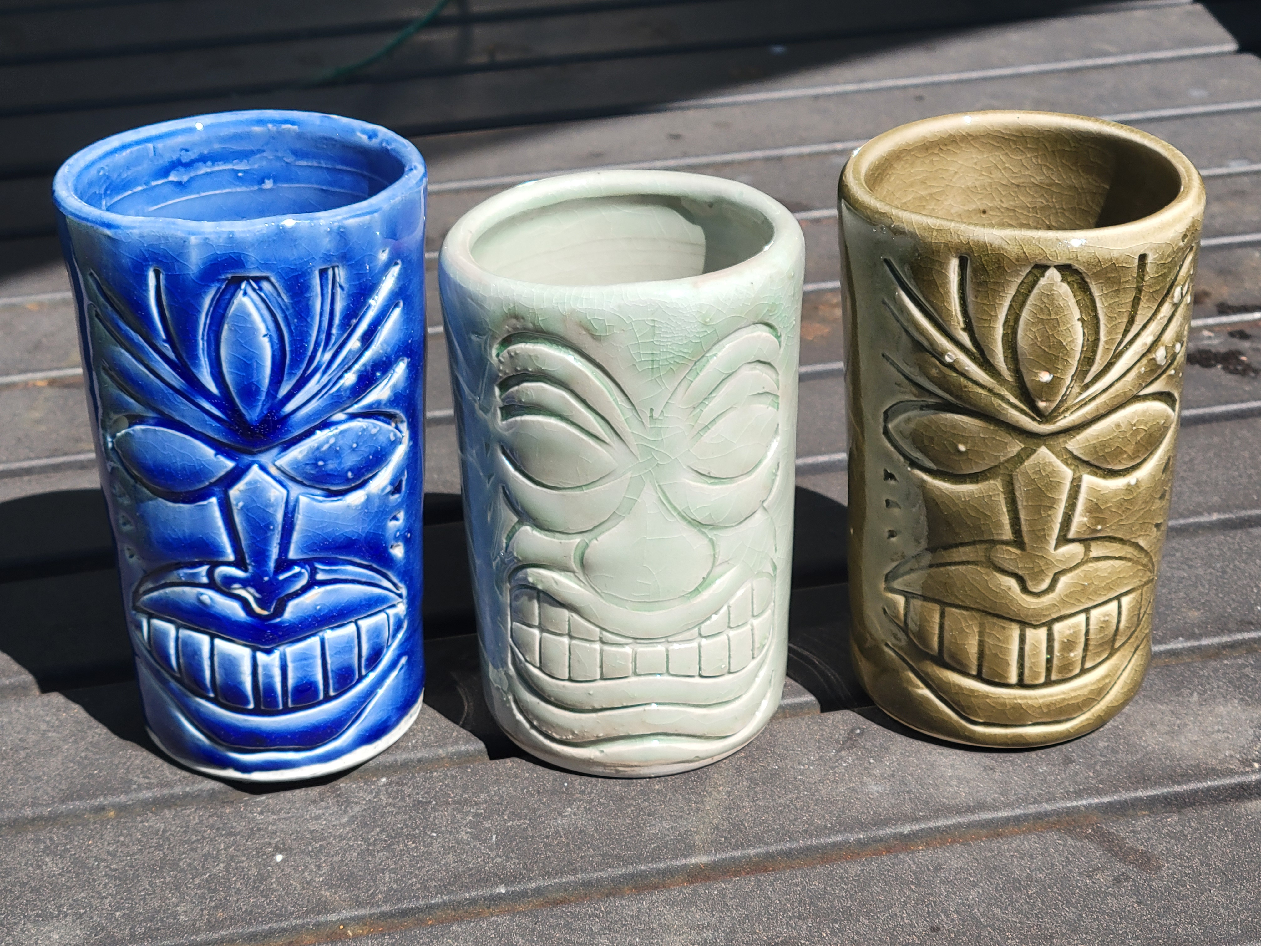 three tiki mugs in green and blue on a table