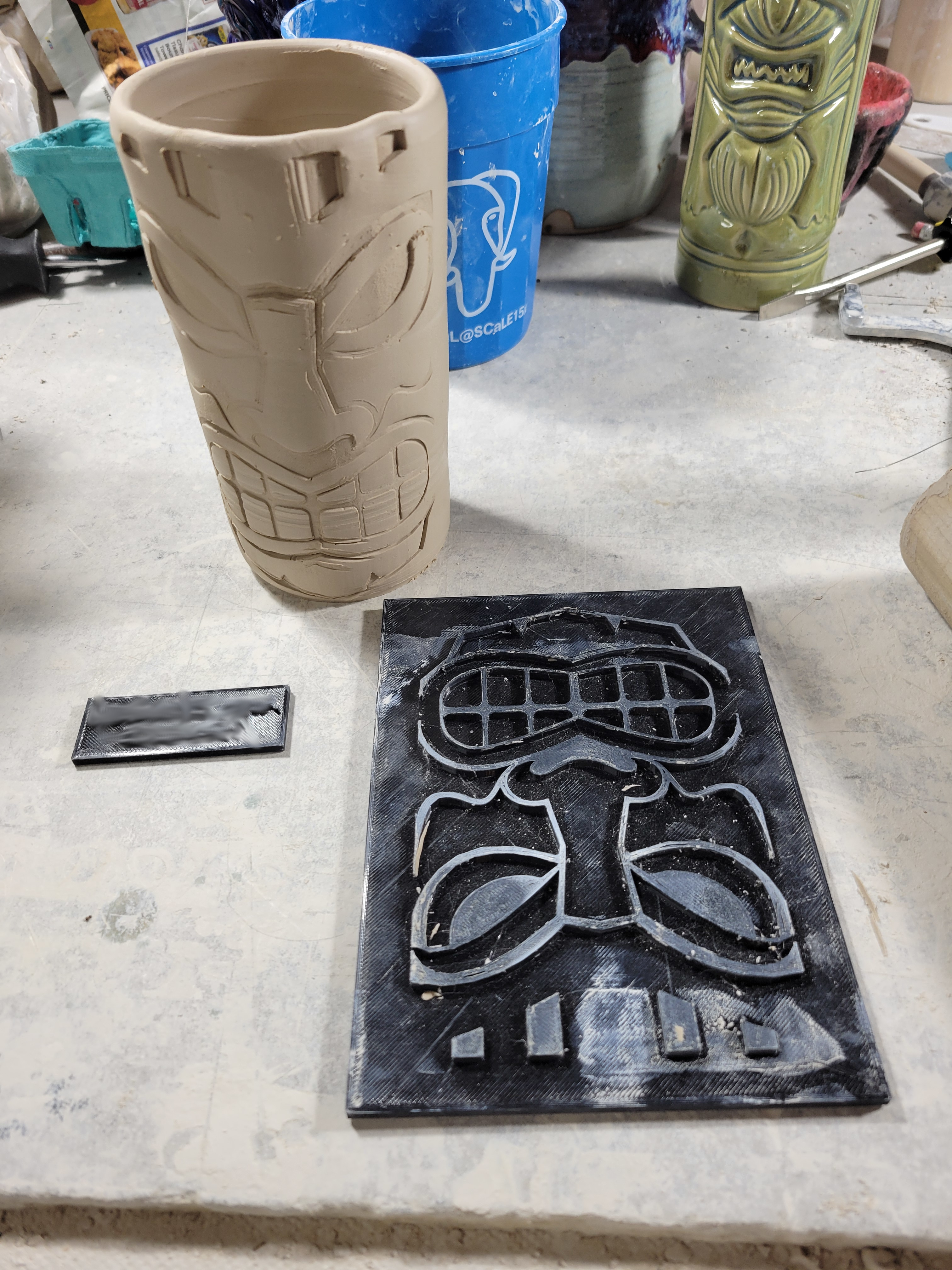 a tiki cup in wet clay next to a texture mat